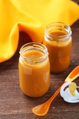 Baby food in bottles with spoon on brown wooden background