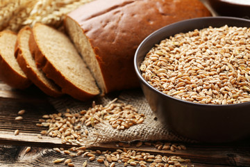 Ears of wheat and bowl of wheat grains on brown wooden backgroun