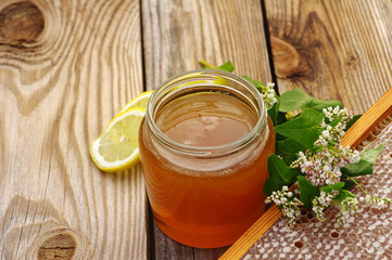 Honey in a glass jar, buckwheat flowers, a lemon and bee honeycombs in a summer sunny day. Honey with flowers and honeycombs