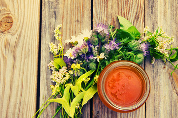 Honey in a glass jar with June flowers melliferous herbson a wooden surface. Honey with flowers