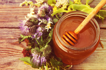 Honey in a glass jar with June flowers melliferous herbson a wooden surface. Honey with flowers