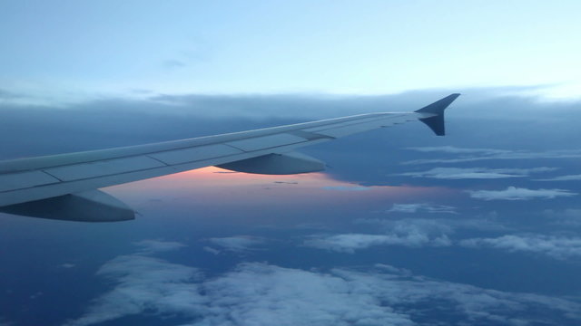 Peaceful View from Plane Window &ndash;&nbsp;Looking out a jet window at a blue cloudscape with the sunset reflecting off water in the distance