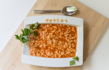horizontal image of a white dish sitting on a wood  cutting board filled with alpha-getti  in tomato sauce with the pasta letters 