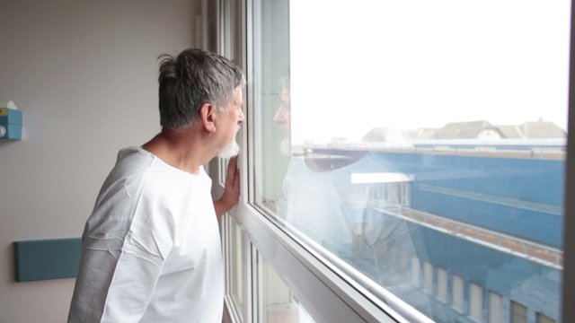 Patient at a hospital, looking from a window in his room, doing much better after the surgery