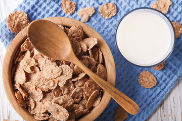 Cereal flakes in a wooden bowl and milk close-up. top view horizontal
