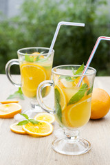Orange fresh drinks with ice and mint on wooden table, selective focus