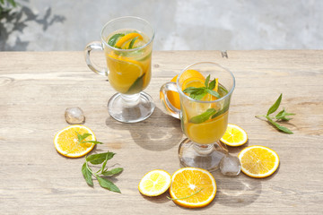 Orange fresh drinks with ice and mint on wooden table, selective focus