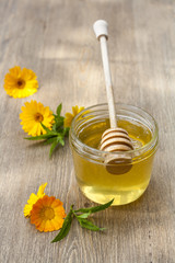 Linden honey in jar and calendula blossoms on wooden table, selective focus
