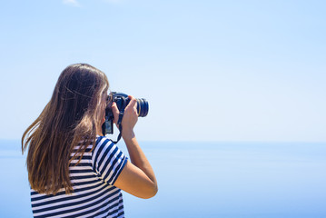 young caucasian female with camera on a cliff, woman taking photos on seaside