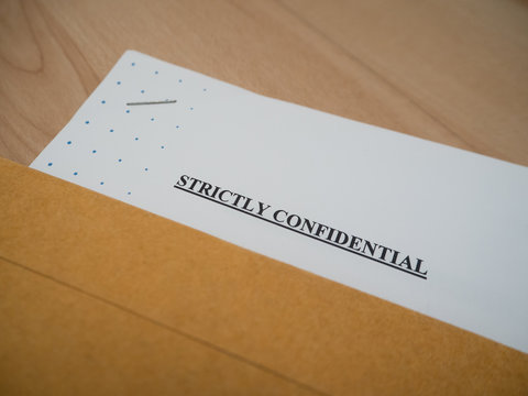 "Strictly Confidential" document in brown vintage envelope on wood table, in macro