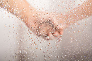 Fototapeta premium Mother's hand holding kid's hand behind the water drop on glass