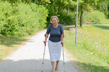 Frau geht im Park an ihren Krücken