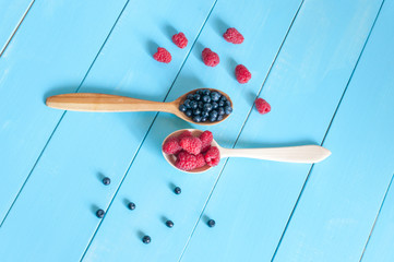 Fresh blueberries and raspberries in wooden spoon. Light blue