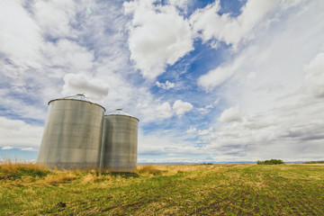 Fototapeta na wymiar Metal grain silos on a prairie landscape with a blue cloudy sky.