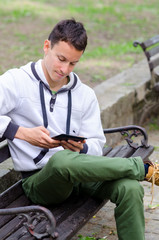 Young man sitting on the bench and using pad device