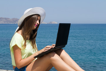 Young girl with laptop, in shorts and white hat outdoors.