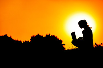 silhouette of a girl with laptop on sunset or sunrise background