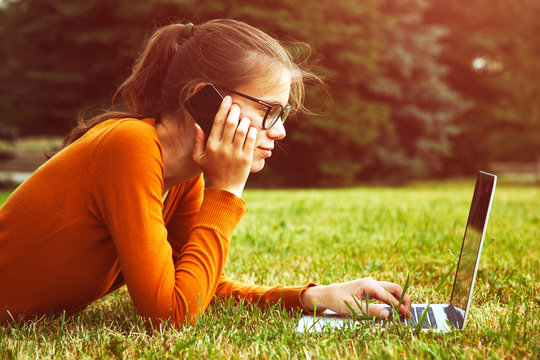 Girl Lying In The Grass And Using Laptop And Smart Phone