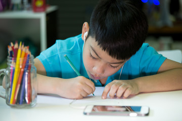 Naklejka premium A boy using cellphone and painting on a white paper at home