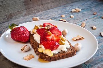 Dark rye bread topped with fresh strawberries, ricotta cheese and pistachio nuts and a drizzle of honey.