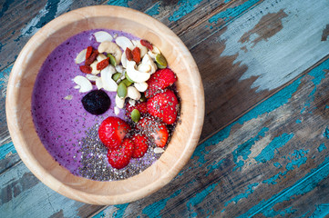 Healthy breakfast fruit smoothie bowl of blueberry and strawberry blended with kefir yogurt and topped with fresh strawberry, chia seeds, goji berries, cashews and pumpkin seeds. - obrazy, fototapety, plakaty