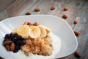 Healthy porridge of quinoa and kefir yogurt served with banana, blueberries, almonds and a sprinkling of chia seeds.Served on a rustic blue wooden table.