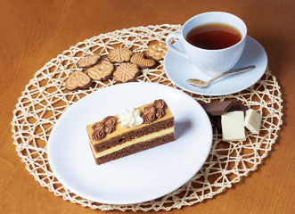 Sweet cake with cup of tea, cookies  and chocolate on wooden tab