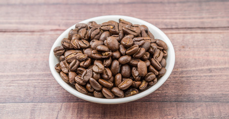 Roasted coffee beans in white bowl over rustic wooden background