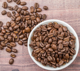 Roasted coffee beans in white bowl over rustic wooden background