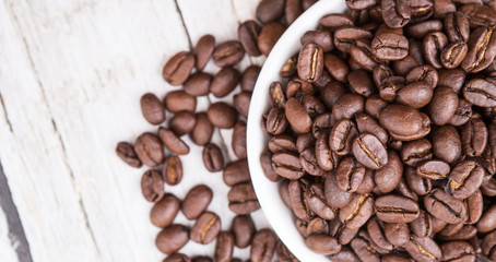 Roasted coffee beans in white bowl over rustic wooden background