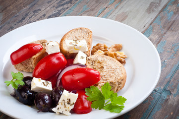 A healthy salad of Greek barley rusks with feta,tomato,onion and walnuts drizzled with olive oil. Served on a rustic wooden table.