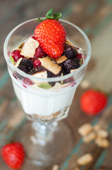 Homemade granola with Greek yoghurt topped with frozen berries, coconut and a fresh strawberry.Served in a tall glass.