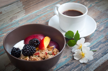 A bowl of healthy breakfast muesli with yogurt and topped with fresh blackberries, sliced nectarine, goji berries, pumpkin seeds and walnuts.Served with fresh coffee and wild flowers.