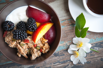A bowl of healthy breakfast muesli with yogurt and topped with fresh blackberries, sliced nectarine, goji berries, pumpkin seeds and walnuts.Served with fresh coffee and wild flowers.