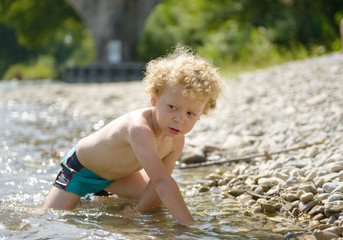 portrait of a young blonde boy playing in water