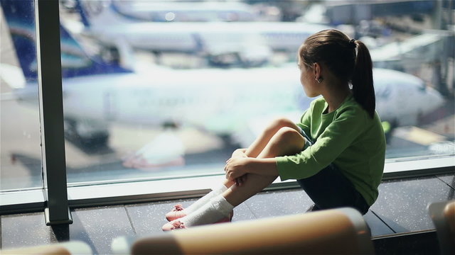 Child at the airport near the window looking at airplanes and waiting for time of flight