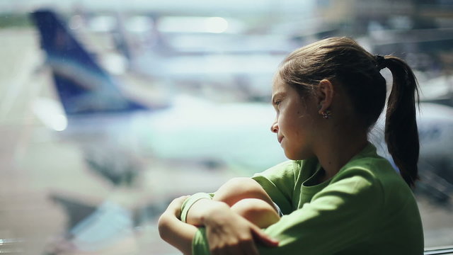 Child at the airport near the window looking at airplanes and waiting for time of flight