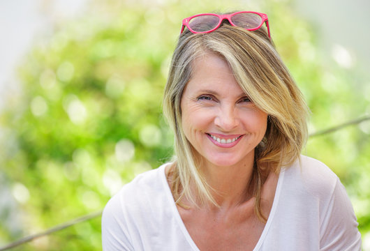 Portrait of charming blond woman of middle-aged smiling in glasses on green background