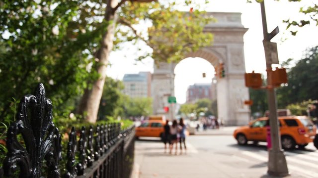 People and cars near Washington Square Arch in Manhattan's Greenwich Village. Focus is on wrought iron fence on left.