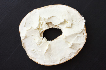 Bagel spread with cream cheese. Isolated on black wood from above.