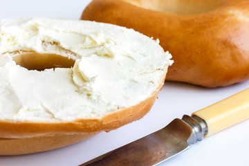 Plain bagel with knife, spread with cream cheese, detail.