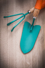 Close up view of metal hand spade and gardening rake on wood boa