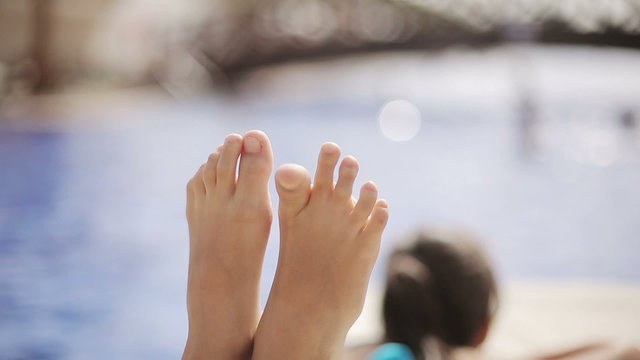Child lies on a sun lounger by the pool at the hotel and moves her feet
