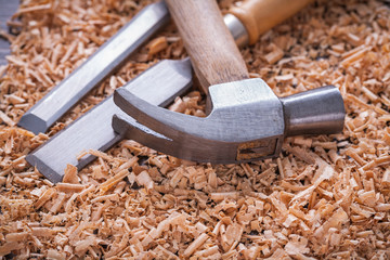 Claw hammer and chisels in wooden shavings on vintage wood board