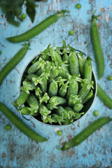 Fresh green peas in a small metal bucket on blue wooden background. Top view.