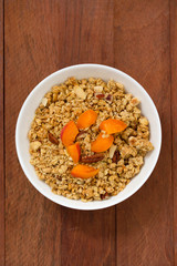 granola with fruits and nuts in white bowl on brown wooden background