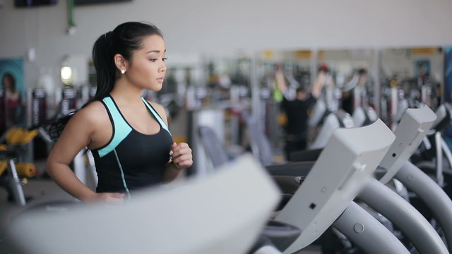 Attractive asian girl running on the treadmill in the gym. Right profile face