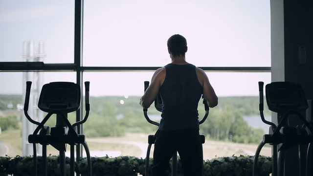 Silhouette of handsome man at the gym exercising on the strainer machine. Dolly shot left to right