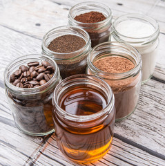 Coffee beans, coffee powder, creamer, cocoa powder, honey and processed tea leaves in a mason jar over weathered wooden background