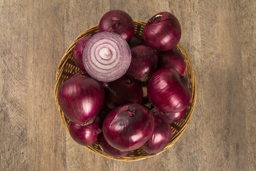 Obraz premium Red onions in a basket and a cut red onion over a table.